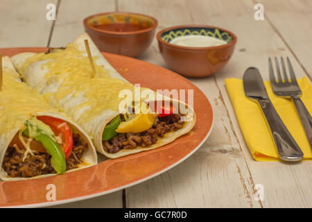 Burrito riempiti con carne macinata di manzo e peperoni conditi con formaggio e salsa crema acida sul lato Foto Stock