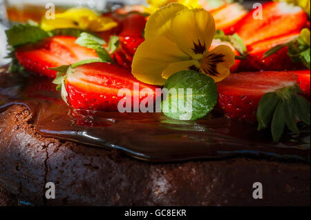 Torta al cioccolato con fragole e fiori eddible close up Foto Stock