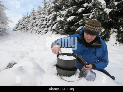 Keith Hollis fa bollire la neve per preparare una tazza di tè durante la stagione festiva, mentre in alto sulle colline della Carron Valley, Scozia centrale. Foto Stock