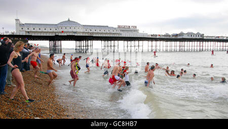I membri del pubblico si dirigono verso il mare ghiacciato per l'annuale Brighton Swimming Club Christmas Day Swim nel resort East Sussex. Foto Stock
