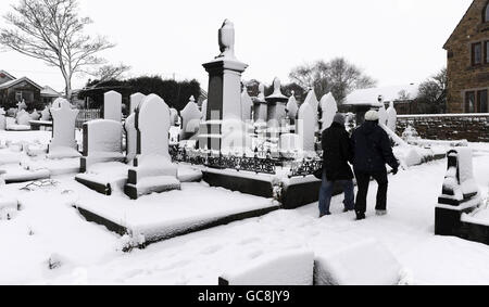 Le lapidi di un cimitero vicino a Huddersfield sono coperte di neve profonda, mentre la neve continua a cadere in molte aree del Regno Unito. Foto Stock