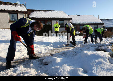 Gli uomini sgorgano la neve da un sentiero in un complesso residenziale protetto, come parte del loro servizio comunitario a Dunfermline. Foto Stock