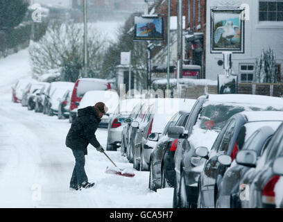 Un uomo libera la neve da tutto il suo automobile in Great Chart vicino Ashford, Kent dopo una notte di caduta pesante della neve. Foto Stock