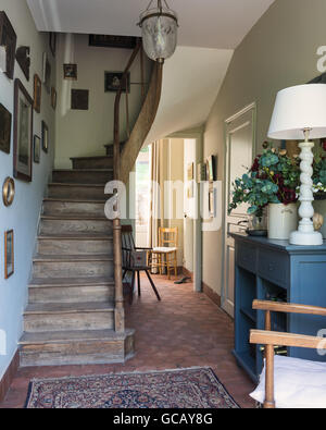 Hall con pavimenti con mattonelle di terracotta, scala di legno e oriental rug Foto Stock