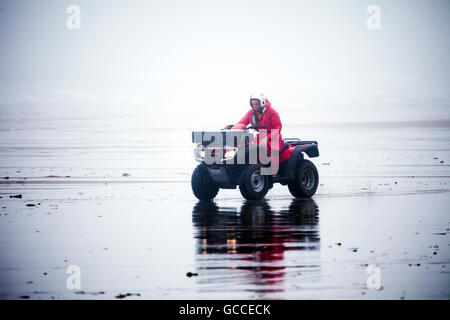 Nebbia estiva su Whitsand Bay, Cornwall, Regno Unito come una guardia RNLI trascina lungo la spiaggia su di una moto quad Foto Stock