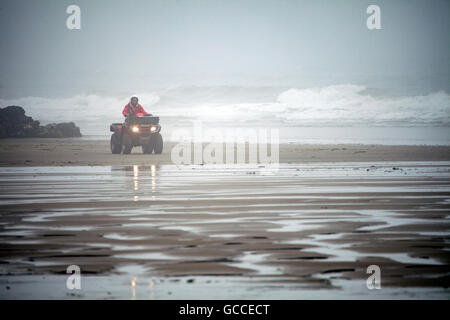 Nebbia estiva su Whitsand Bay, Cornwall, Regno Unito come una guardia RNLI trascina lungo la spiaggia su di una moto quad Foto Stock