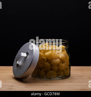 Pasta cruda in un vasetto di vetro con tappo grigio sul tavolo di legno Foto Stock