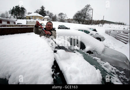 Un uomo libera la neve da un'auto vicino a Denny, Scozia centrale, dopo una notte di nevicate. Foto Stock