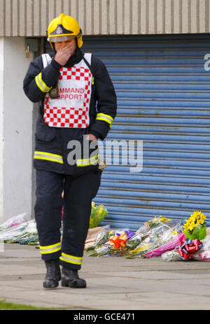 Un combattente del fuoco cammina attraverso i fiori ai piedi delle Shirley Towers a Southampton, dopo che i vigili del fuoco Alan Bannon e James Shears sono stati uccisi durante un incendio al blocco di appartamenti nella zona di Shirley della città durante la notte. Foto Stock