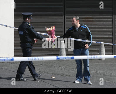 Un membro del pubblico passa fiori a un Garda fuori dal pub Faussagh House a nord di Dublino dove Eamon Dunne, 32 anni, da Dunsinghly Drive a Finglas, è stato ucciso. Foto Stock