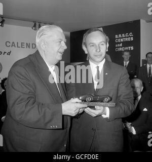 John Surtees, campione del mondo in carica, sorride in quanto, a nome del British Racing and Sports Car Club, ha ricevuto un trofeo da Herr Alfred Neubauer, team manager della scuderia Mercedes-Benz dal 1925 al 1955, quando il 6° Racing Car Show ha aperto a Olympia. Foto Stock