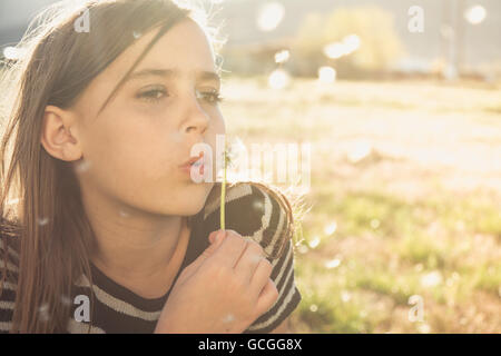 11 anno vecchia ragazza soffiando tarassaco semi. Foto Stock
