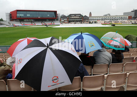 Gli spettatori prendono la copertura sotto i loro ombrelli come la pioggia copre Vieni a Old Trafford Foto Stock