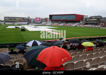 Cricket - Npower secondo Test - Day Three - Inghilterra / Bangladesh - Old Trafford. Gli spettatori si coprono sotto i loro ombrelloni mentre le coperture per la pioggia si accendono a Old Trafford Foto Stock