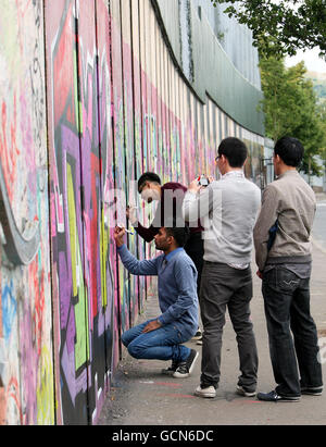 I turisti scrivono messaggi sul Muro della Pace a Belfast. I capi del turismo hanno colpito oggi dopo che gli australiani sono stati invitati dal loro governo a prestare attenzione alla minaccia repubblicana dissidente nell'Irlanda del Nord. Foto Stock