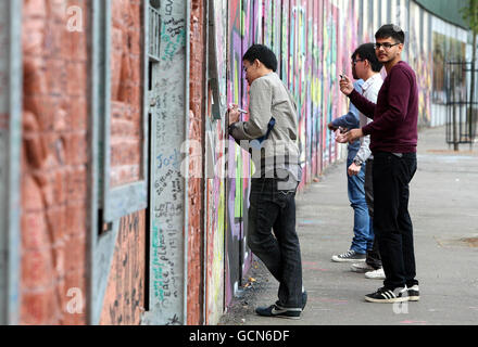 I turisti scrivono messaggi sul Muro della Pace a Belfast. I capi del turismo hanno colpito oggi dopo che gli australiani sono stati invitati dal loro governo a prestare attenzione alla minaccia repubblicana dissidente nell'Irlanda del Nord. Foto Stock