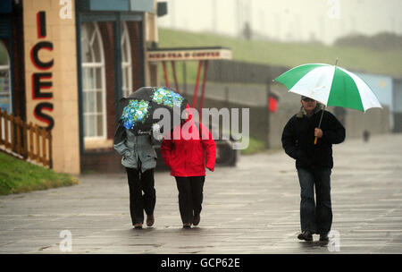 Gli escursionisti si riparano sotto gli ombrelloni sulla Whitley Bay Promenade, North Tyneside, mentre il tempo umido continua in tutto il Regno Unito. Foto Stock