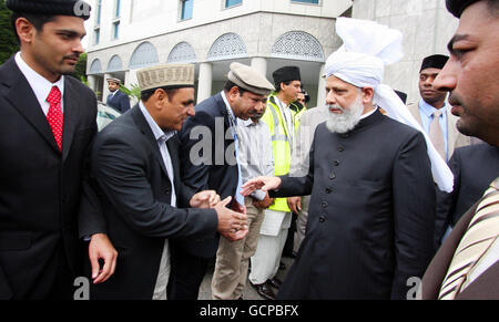 ahmadi musulmani alla Moschea di Baitul Futuh a Morden, Londra, la più grande moschea dell'Europa occidentale, dopo aver celebrato Eid con la preghiera, in cui oltre 10,000 fedeli hanno ricevuto un sermone Eid vivo dal capo mondiale della comunità musulmana Ahmadiyya, sua Santità, Hadhrat Miza Masroor Ahmad, (a destra), indossando un turbante. Foto Stock