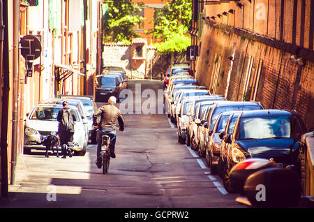 Bologna, Italia uomo calvo cross street con la bicicletta a fianco di una fila di automobili parcheggiate Foto Stock