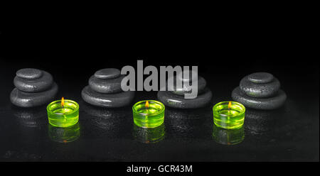 Spa concept della piramide zen pietre di basalto con gocce di acqua e candele verdi su sfondo nero, close up Foto Stock