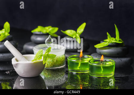 Spa sfondo della piramide zen pietre di basalto con gocce d'acqua, la menta, il sale marino, mortaio e pestello di candele Verde su nero, vicino u Foto Stock