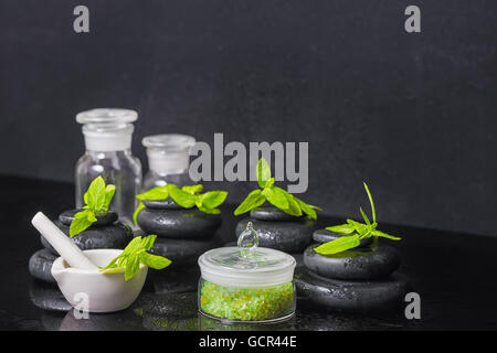 Spa sfondo della piramide zen pietre di basalto con gocce d'acqua, la menta, il sale marino, mortaio e pestello di bottiglie di tintura su nero, c Foto Stock