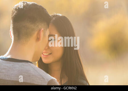 Una giovane coppia asiatica godendo del tempo di qualità insieme in un parco in autunno e che abbraccia ogni altra nel tepore del sole serale Foto Stock