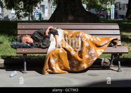 Sofia, Bulgaria - 6 Luglio 2016: donna senzatetto è dormire su un banco in un parco avvolto in una coperta nel centro di Sofia. Anni Foto Stock