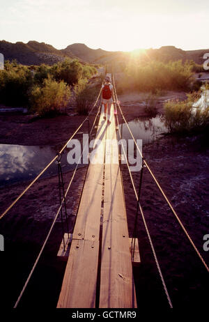 Escursionista femmina attraversando ponte pedonale al tramonto; Southern Utah deserto; USA Foto Stock