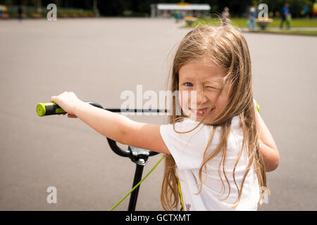 Ritratto di bella felice bambina su uno scooter in un parco Foto Stock