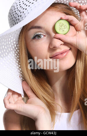 Ritratto di giovane adulto donna caucasica su sfondo bianco azienda fette di cetriolo sopra i suoi occhi. Foto Stock