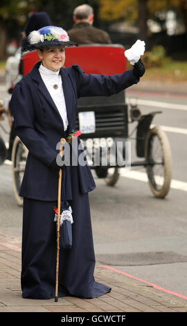 Una donna in costume d'epoca ondeggia come partecipanti a Londra a Brighton Veteran Car Run guidare su Brixton Hill, nel sud di Londra. Foto Stock