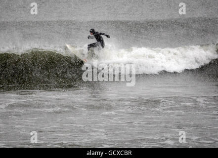 Un surfista affronta le condizioni meteorologiche gelide nell'inseguimento del suo sport alla spiaggia di Aberdeen, Scozia, come più nevicate sono previste per gran parte del Regno Unito. Foto Stock