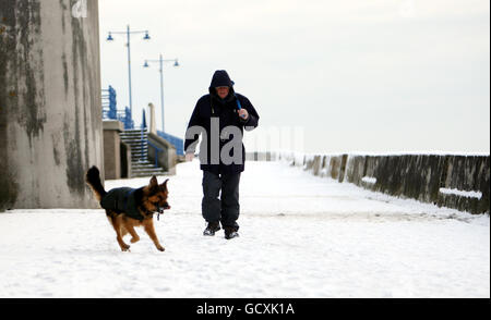 Collin Woods e il suo cane Zeb fare una passeggiata innevata sul lungomare di Porthcawl, Galles meridionale. Foto Stock