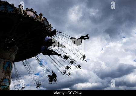 Le persone godono di fiera carosello ride contro il cielo scuro sfondo Foto Stock