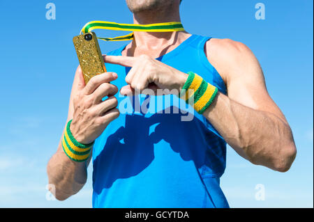 Atleta brasiliano con il giallo e il verde del Brasile di braccialetti a colori utilizzando la medaglia d'oro telefono mobile contro il cielo blu Foto Stock