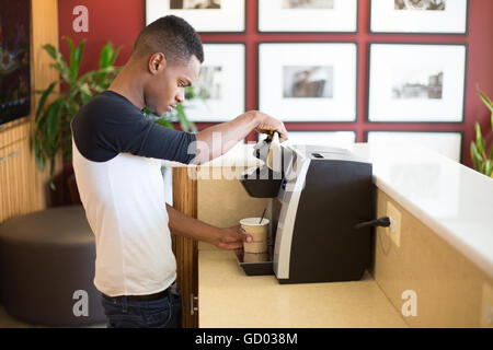 Closeup Ritratto, giovane ragazzo rendendo caldo o caffè ghiacciato con la macchina, isolata all'interno di fondo interna. Lunedì mattina Foto Stock