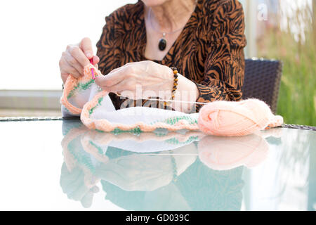 Primo piano ritagliato ritratto di donna vecchia mani, seduta e panno a crochet con aghi arancio, isolato all'aperto sullo sfondo Foto Stock