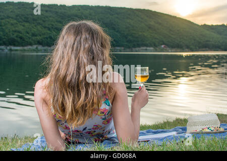 Donna con un bicchiere di vino in riva al lago Foto Stock