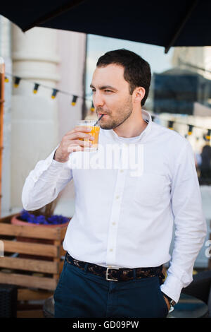 Bel giovane azienda di vetro di colore arancione del succo di frutta fresco e sorridente, all'aperto Foto Stock