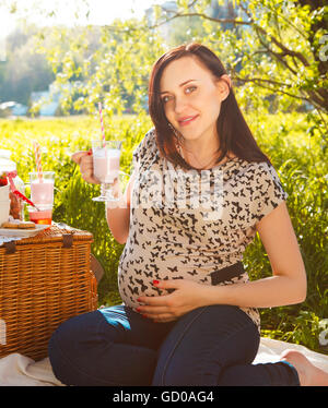 Ritratto di bella donna incinta bere latte shake al picnic nel parco di primavera Foto Stock