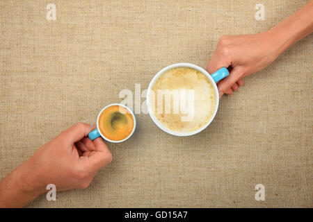 Due mani, uomo e donna, azienda espresso ristretto e big cappuccino cappuccino tazze da caffè insieme su tela di lino sfondo Foto Stock