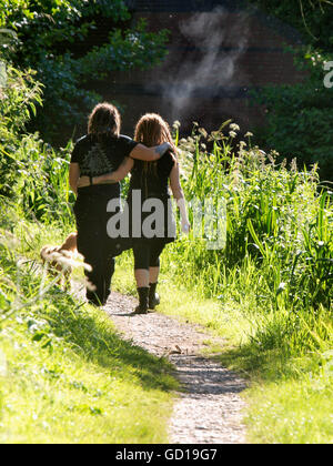 Coppia giovane a piedi lungo un sentiero, braccia attorno ad ogni altro in estate il sole, Devizes, Wilts, Regno Unito Foto Stock