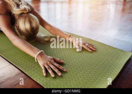 Femmina facendo stretching allenamento sul tappeto di esercizio. Donna balasana facendo yoga in palestra, con focus sulle mani. Foto Stock