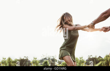 Colpo di attraente giovane donna tenendo le mani dell uomo e la danza nel prato. Giovane godendo all'aperto nel campo. Foto Stock