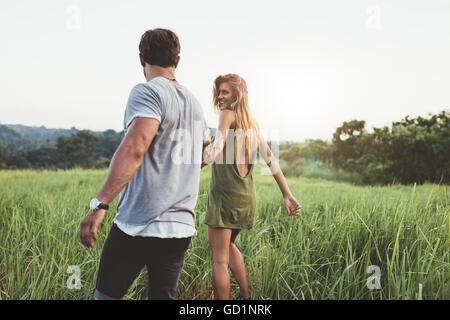 Vista posteriore del colpo di giovane donna che cammina con il suo fidanzato sul campo in erba. Giovane godendo di una passeggiata attraverso la terra di erba. Foto Stock