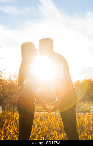 Una giovane coppia asiatica baciare in un parco in autunno e facendo un cuore con le loro mani nel tepore del sole al tramonto; Edmonton, Alberta, Canada Foto Stock