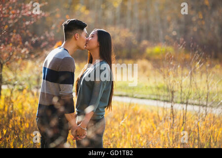 Una giovane coppia asiatica godendo Di Un tempo romantico insieme all'aperto in Un parco in autunno e baciarsi l'un l'altro nel calore della luce del sole... Foto Stock