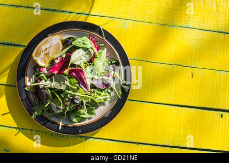 Insalata primaverile di baby spinaci, erbe aromatiche, rucola e lattuga sulla tabella di colore giallo Foto Stock