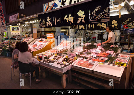 Diners sedersi e parlare con frutti di mare proprietario di stallo, Omicho cibi freschi di mercato, rete di coperta rivestita di stallo strade, Kanazawa, Giappone Foto Stock